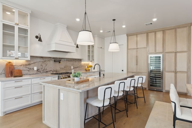 kitchen featuring sink, range, a center island with sink, custom exhaust hood, and beverage cooler