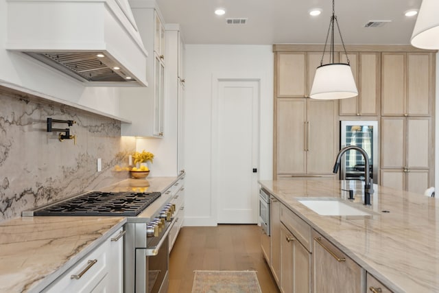 kitchen with premium range hood, decorative light fixtures, sink, stainless steel appliances, and light stone countertops