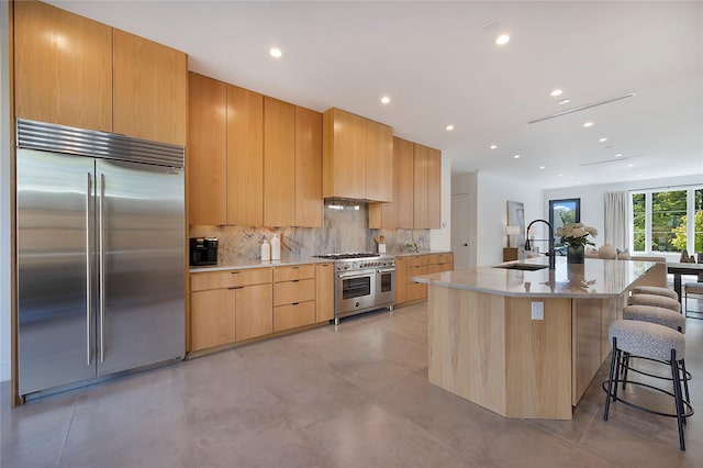 kitchen with a center island with sink, decorative backsplash, sink, high end appliances, and a breakfast bar area