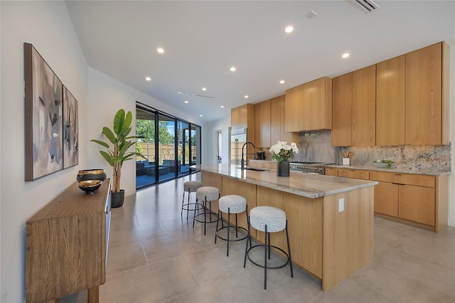 kitchen featuring a kitchen bar, a large island, tasteful backsplash, light stone counters, and sink