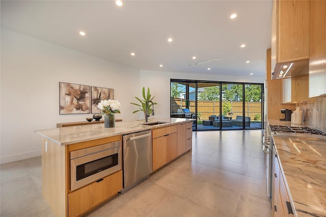 kitchen with light stone countertops, stainless steel appliances, light brown cabinetry, sink, and a center island with sink