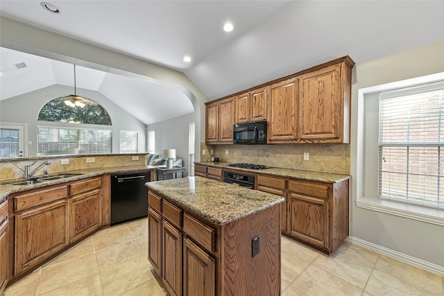 kitchen featuring light stone counters, sink, black appliances, and a center island