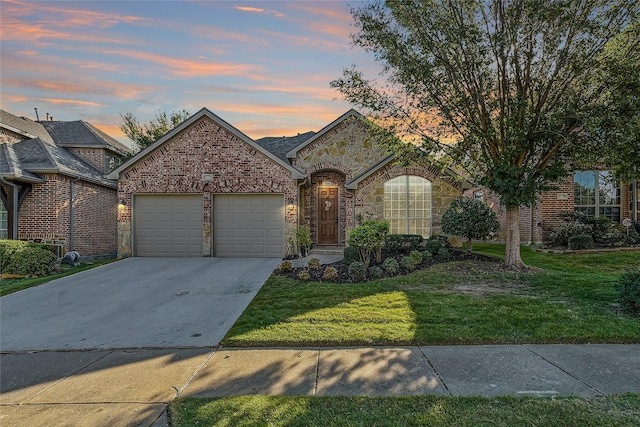 french provincial home featuring driveway, stone siding, a yard, an attached garage, and brick siding