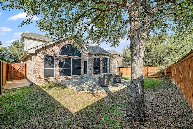 rear view of house with brick siding, a fenced backyard, a yard, a patio, and a gate