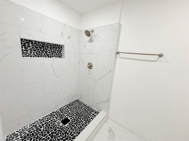 bathroom featuring baseboards, marble finish floor, and a tile shower