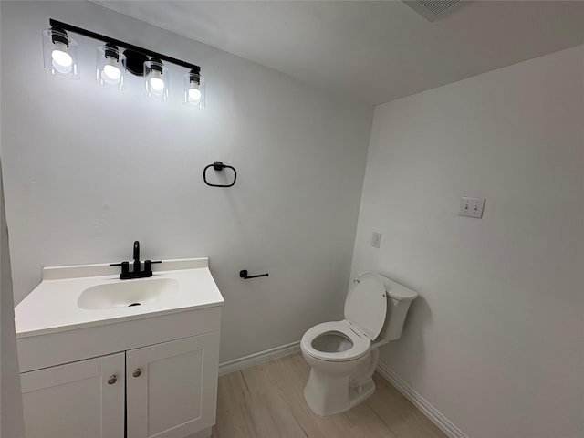 half bathroom featuring visible vents, baseboards, toilet, wood finished floors, and vanity