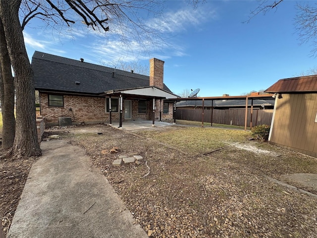 back of property featuring a patio, fence, a shingled roof, a chimney, and brick siding