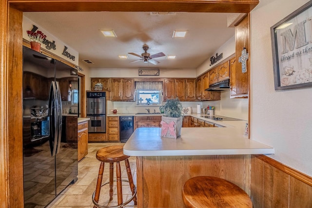 kitchen with kitchen peninsula, a breakfast bar area, ceiling fan, black appliances, and sink