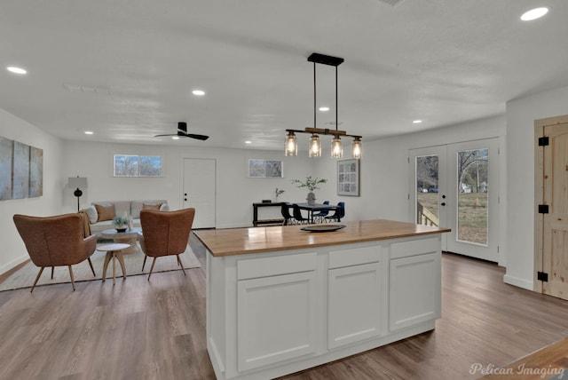 kitchen with wood counters, white cabinetry, ceiling fan, decorative light fixtures, and a center island