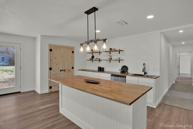 kitchen featuring decorative light fixtures, wooden counters, a center island, sink, and white cabinetry