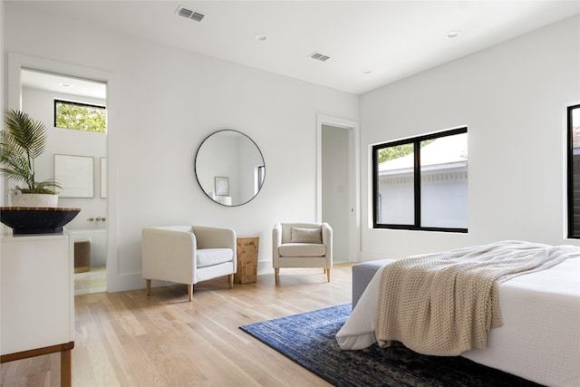 bedroom with ensuite bathroom, light hardwood / wood-style flooring, and multiple windows