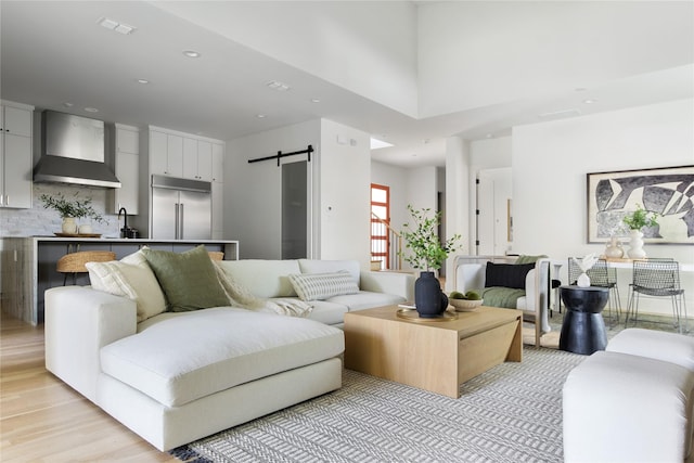 living room featuring a barn door, sink, a high ceiling, and light hardwood / wood-style flooring