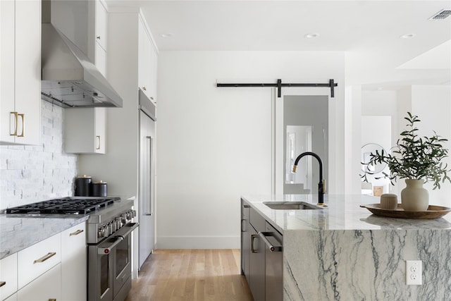 kitchen with high end stainless steel range oven, a barn door, wall chimney exhaust hood, white cabinets, and sink