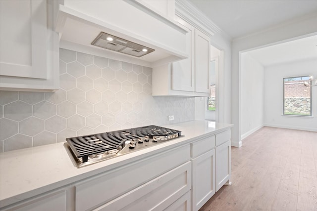 kitchen with decorative backsplash, white cabinets, light hardwood / wood-style flooring, and stainless steel gas cooktop