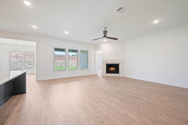 unfurnished living room featuring ceiling fan with notable chandelier, light hardwood / wood-style flooring, and crown molding