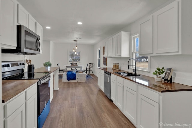 kitchen featuring pendant lighting, sink, white cabinetry, light wood-type flooring, and stainless steel appliances