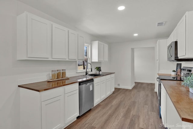 kitchen with sink, white cabinetry, butcher block countertops, and stainless steel appliances