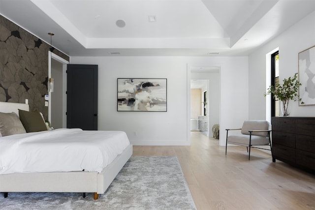 bedroom with light hardwood / wood-style floors and a raised ceiling