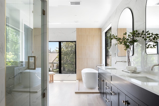 bathroom featuring independent shower and bath, tile walls, hardwood / wood-style flooring, and vanity