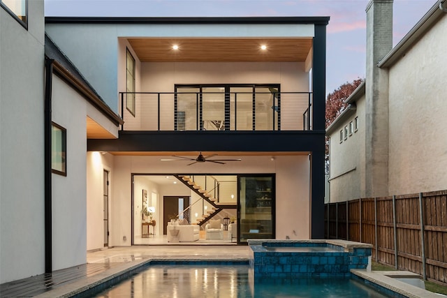 back house at dusk featuring ceiling fan, a pool with hot tub, and a balcony