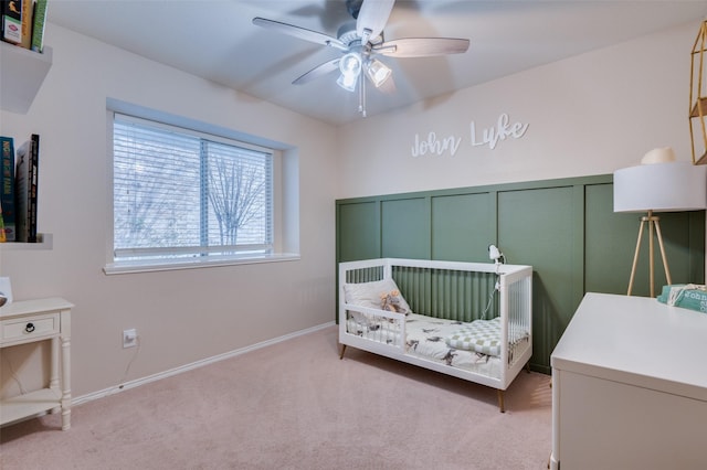 bedroom featuring ceiling fan, a nursery area, and light carpet