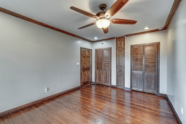 unfurnished bedroom with ceiling fan, multiple closets, dark hardwood / wood-style floors, and crown molding