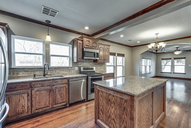 kitchen with a kitchen island, decorative light fixtures, stainless steel appliances, sink, and backsplash