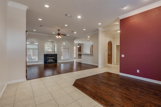 unfurnished living room with ceiling fan, ornamental molding, a tiled fireplace, and light tile patterned flooring