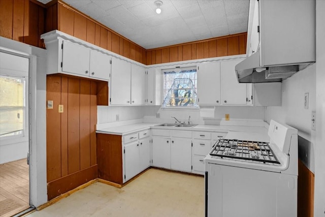 kitchen featuring white range with gas stovetop, sink, wood walls, and white cabinetry