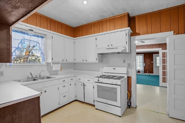 kitchen featuring white gas range, white cabinets, wooden walls, and sink