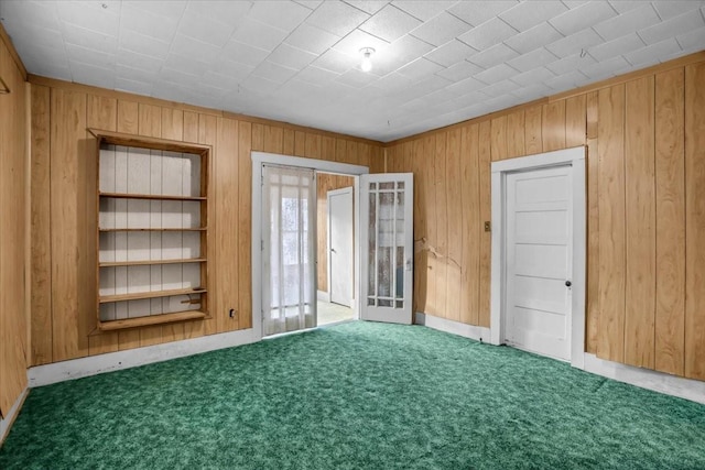 unfurnished room with french doors, wood walls, and dark colored carpet