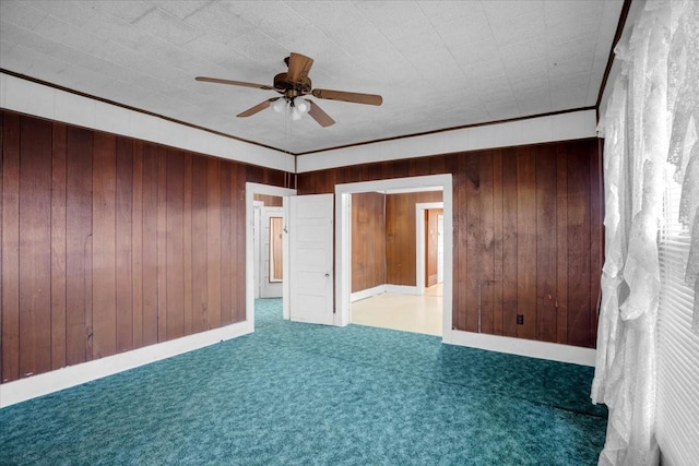 empty room featuring ceiling fan, dark carpet, wooden walls, and ornamental molding