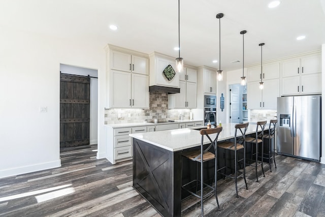 kitchen with appliances with stainless steel finishes, decorative light fixtures, a barn door, a kitchen island with sink, and a breakfast bar area