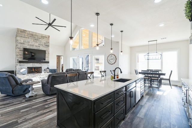 kitchen with a center island with sink, sink, hanging light fixtures, light stone countertops, and a stone fireplace