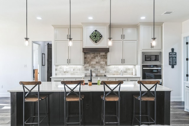 kitchen featuring pendant lighting, a large island with sink, black appliances, dark wood-type flooring, and light stone counters