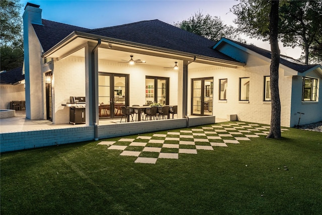 back house at dusk featuring ceiling fan, french doors, a patio area, and a yard