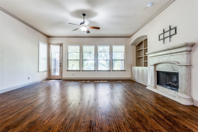 unfurnished living room with ceiling fan, built in shelves, dark hardwood / wood-style flooring, and crown molding