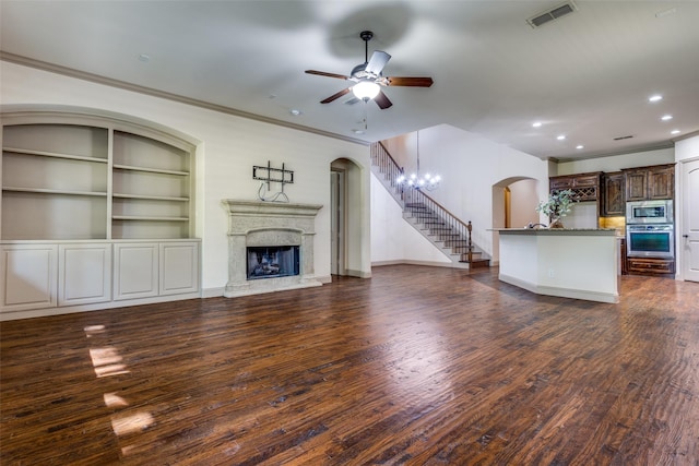 unfurnished living room featuring ornamental molding, ceiling fan with notable chandelier, dark hardwood / wood-style floors, and built in shelves