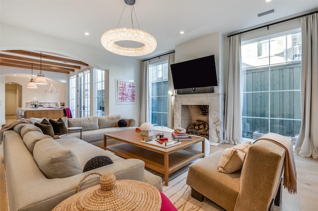 living room with light hardwood / wood-style floors, plenty of natural light, a high end fireplace, and beam ceiling