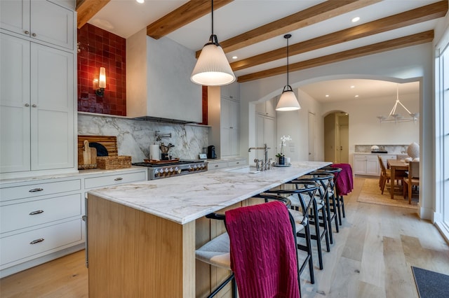 kitchen featuring pendant lighting, an island with sink, white cabinets, a kitchen breakfast bar, and stove