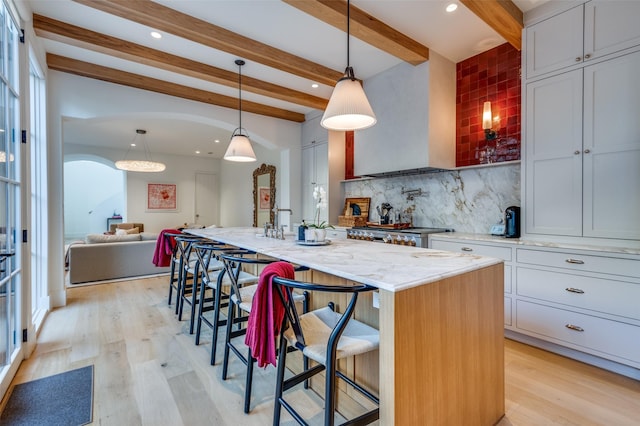 kitchen featuring a kitchen bar, pendant lighting, a center island with sink, and beamed ceiling