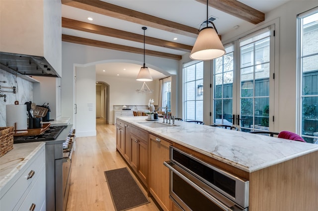 kitchen with a center island with sink, pendant lighting, beamed ceiling, sink, and white cabinetry