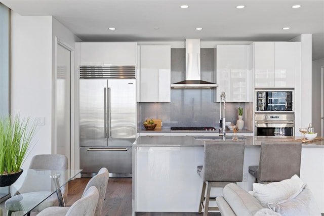 kitchen with white cabinetry, wall chimney range hood, dark hardwood / wood-style flooring, built in appliances, and tasteful backsplash