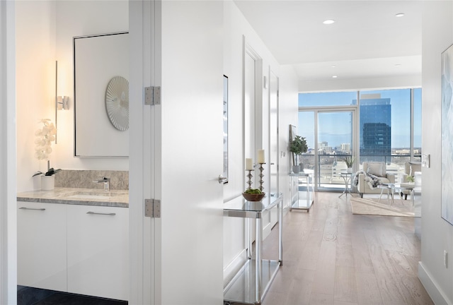 hallway with a wall of windows, sink, and light hardwood / wood-style floors