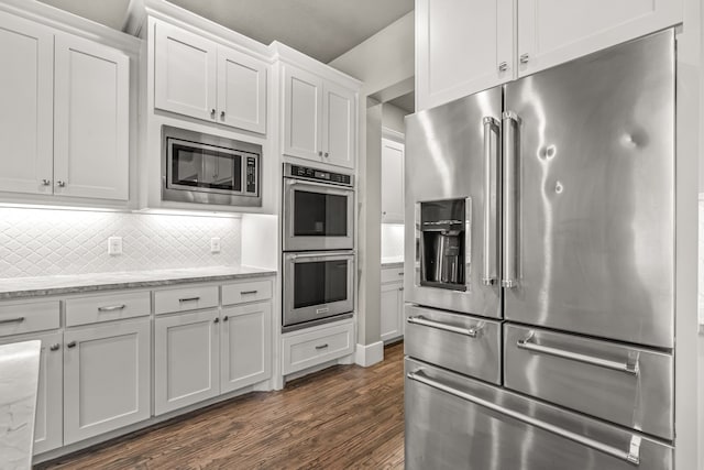 kitchen featuring backsplash, dark hardwood / wood-style floors, white cabinetry, light stone countertops, and appliances with stainless steel finishes