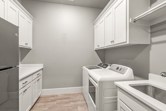 washroom featuring cabinets, light hardwood / wood-style floors, washing machine and clothes dryer, and sink