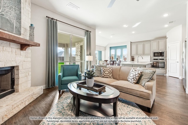 living room with ceiling fan, plenty of natural light, a fireplace, and dark hardwood / wood-style floors