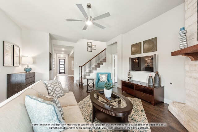 living room featuring ceiling fan, dark hardwood / wood-style flooring, and a stone fireplace