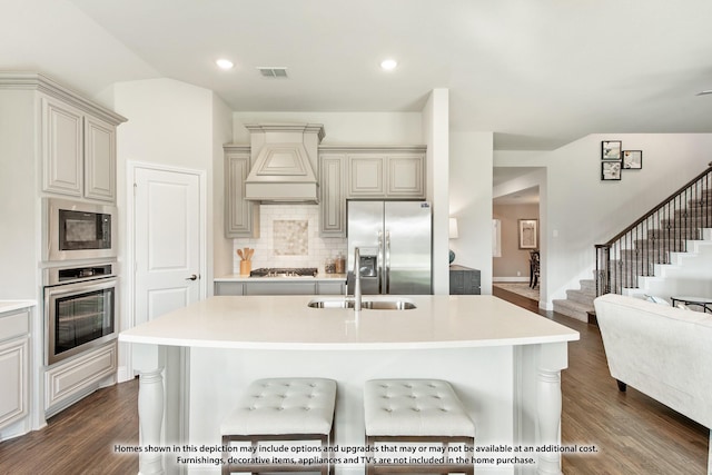 kitchen with premium range hood, an island with sink, appliances with stainless steel finishes, dark hardwood / wood-style floors, and sink