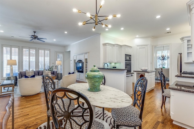 dining room with ceiling fan with notable chandelier, a healthy amount of sunlight, crown molding, and light hardwood / wood-style floors